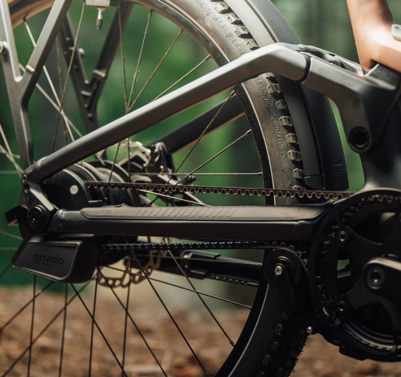 Close-up of a bicycle’s rear wheel and belt drive on a forest trail.
