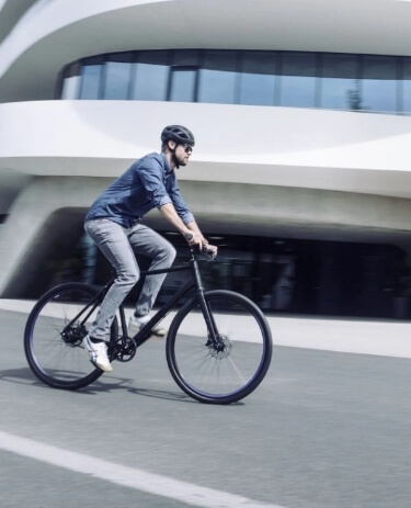 Person fährt mit einem modernen Citybike an einem großen, geschwungenen, futuristischen Gebäude an einem hellen Tag vorbei.