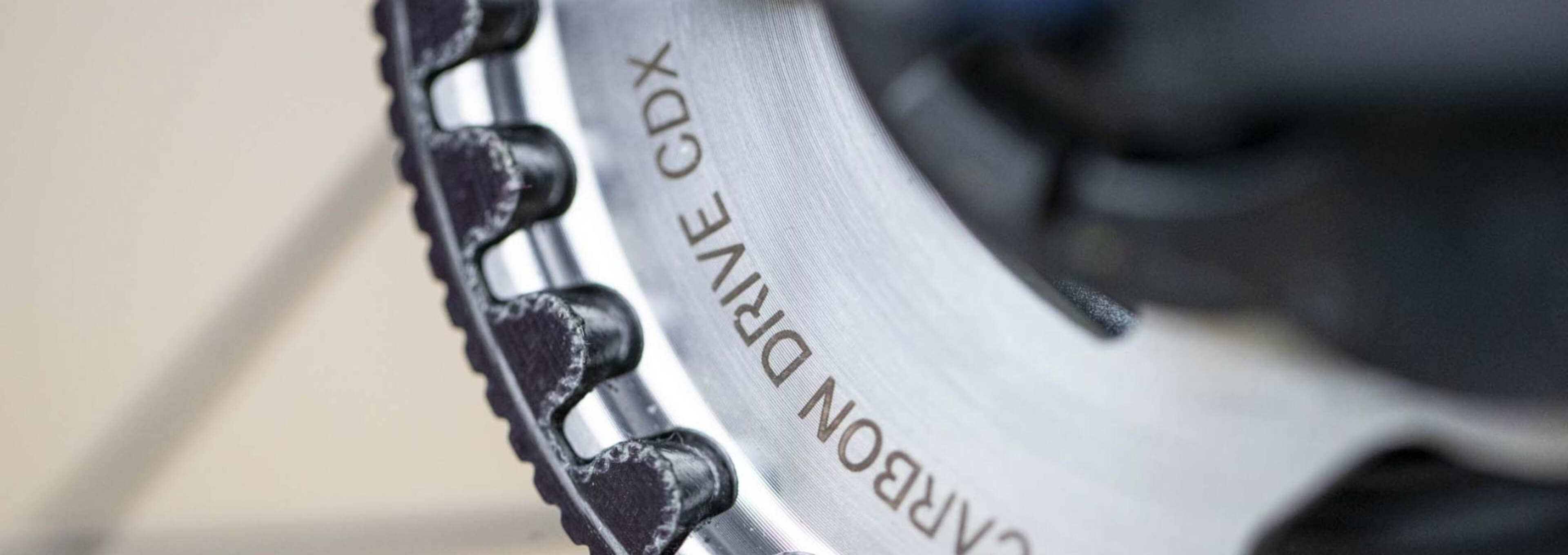 Nahaufnahme eines Fahrrad-Riemenantriebsritzels mit der Gravur „CARBON DRIVE CDX“ auf dem Metallring.