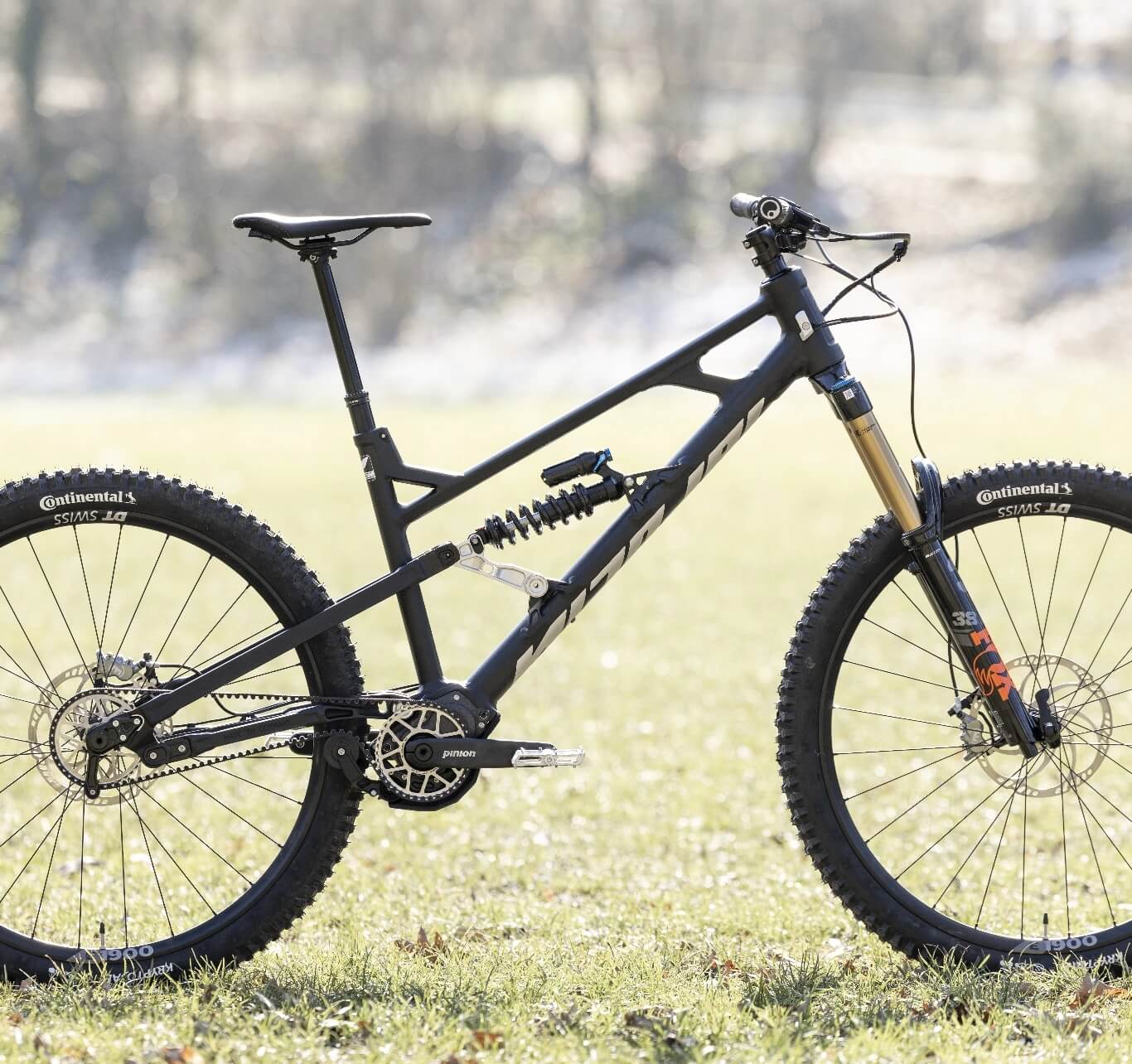Full-suspension black mountain bike with thick off-road tires, standing on grass outdoors.