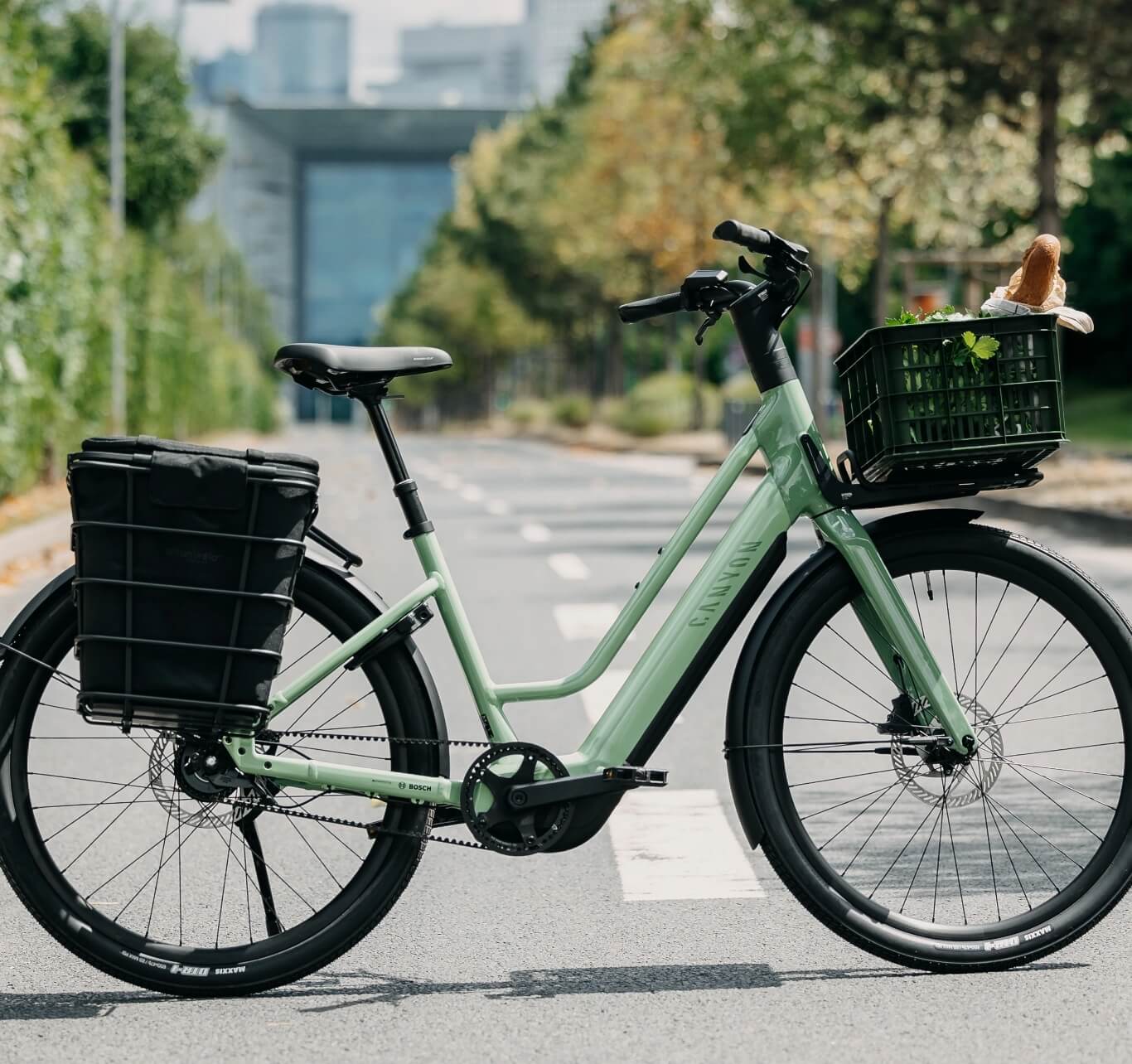 Grey electric city bike with front basket and rear rack standing on an empty street.
