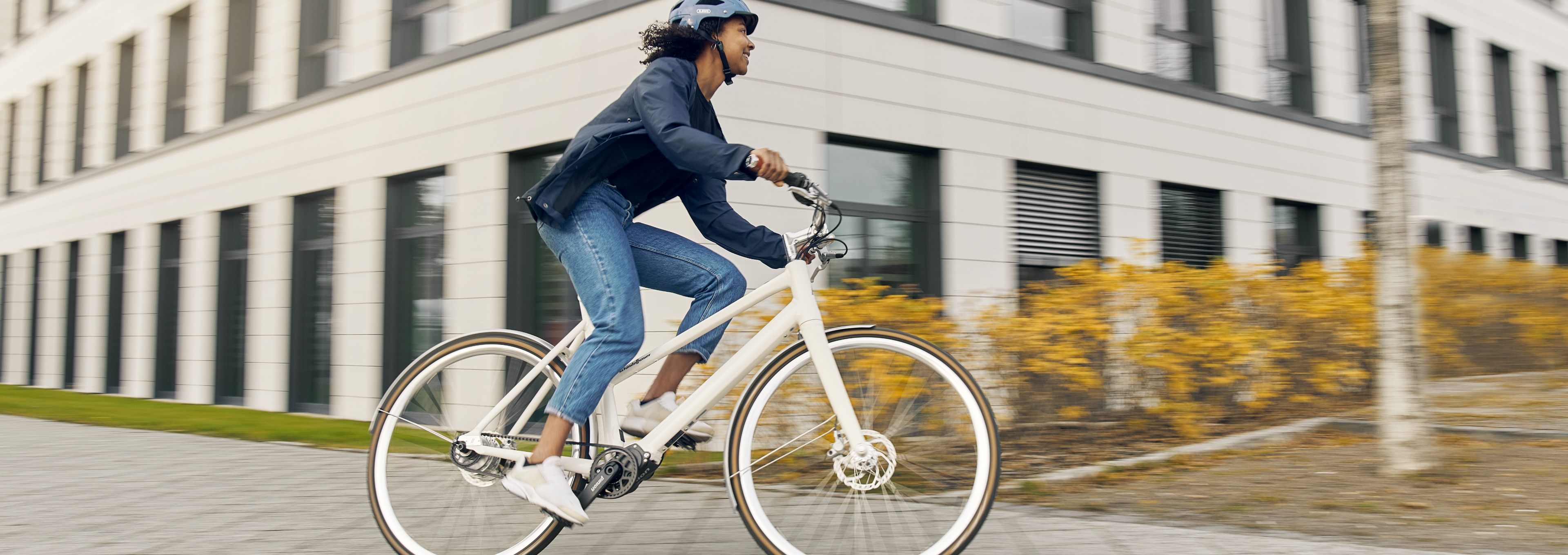 Person mit Helm fährt auf einem weißen Fahrrad an einem modernen Bürogebäude vorbei.