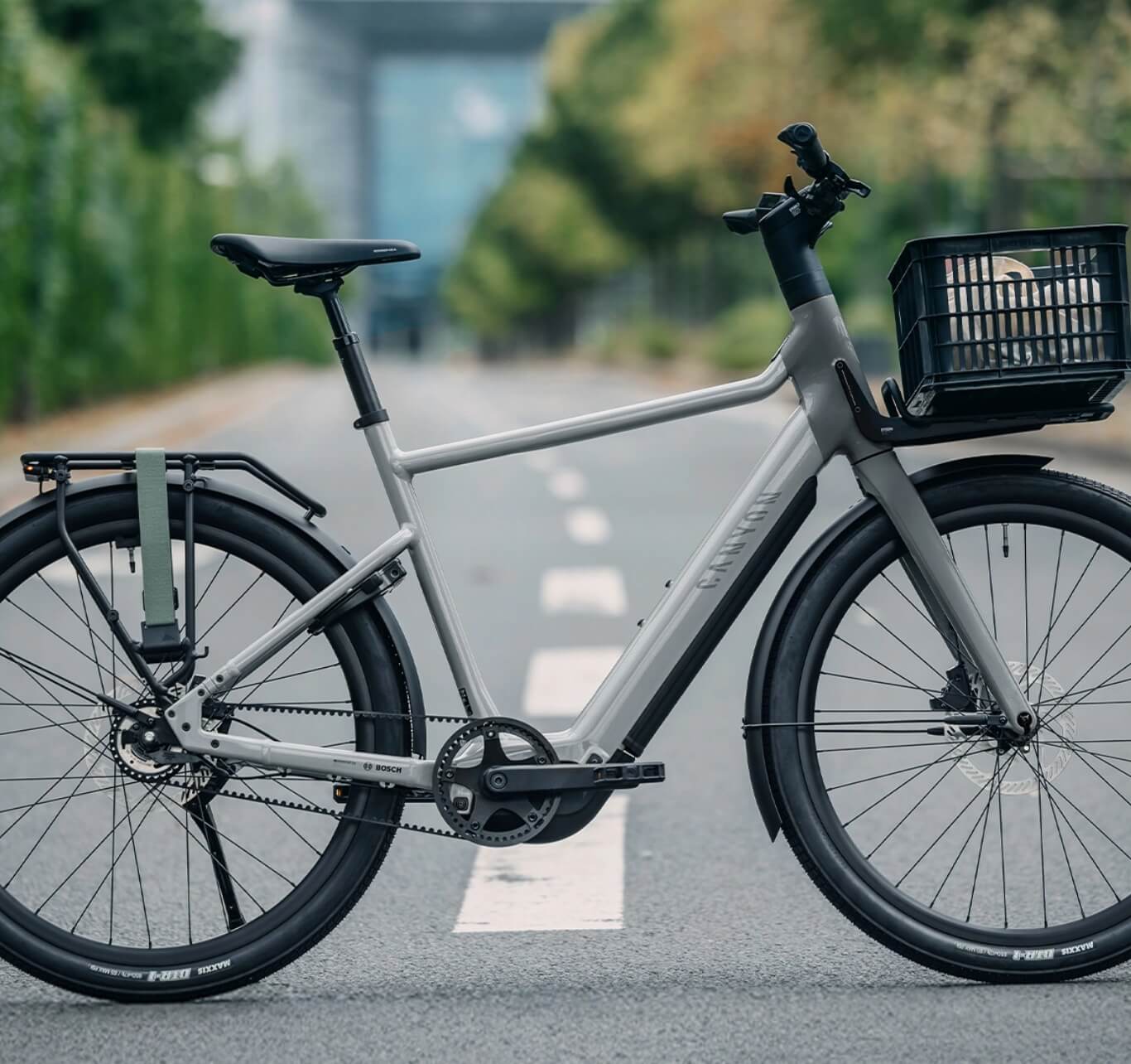 Grey electric city bike with front basket and rear rack standing on an empty street.
